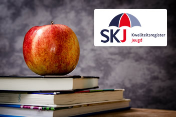 Een stapeltje boeken, een appel én het logo van SKJ Kwaliteitsregister Jeugd voor een schoolbord