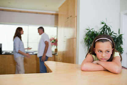 Verdrietig meisje aan tafel, met ouders in conflict op de achtergrond