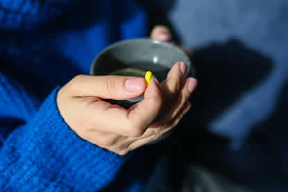 Vrouw in blauwe trui met een kop thee en medicijn in haar handen